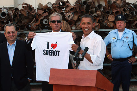 Datuk Bandar Sderot, Eli Moyal menyerahkan t-shirt kepada Barack Obama sambil disaksikan Menteri Pertahanan Israel, Ehud Barak (kiri) sejurus selepas memeriksa roket buatan Palestin semasa lawatannya ke Bandar di selatan Israel itu pada tahun lepas.